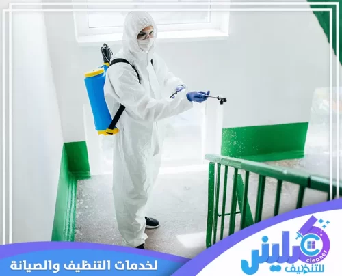 فني مكافحة الحشرات بالمدينة المنورة أثناء رش المبيدات في زاوية درج داخلي، مرتديًا بدلة واقية ويحمل مرشة كبيرة، مما يشير إلى تنفيذ عملية مكافحة شاملة للمبنى. تبرز الصورة أهمية معالجة المناطق المشتركة مثل السلالم لضمان بيئة خالية من الآفات في المدينة المنورة.