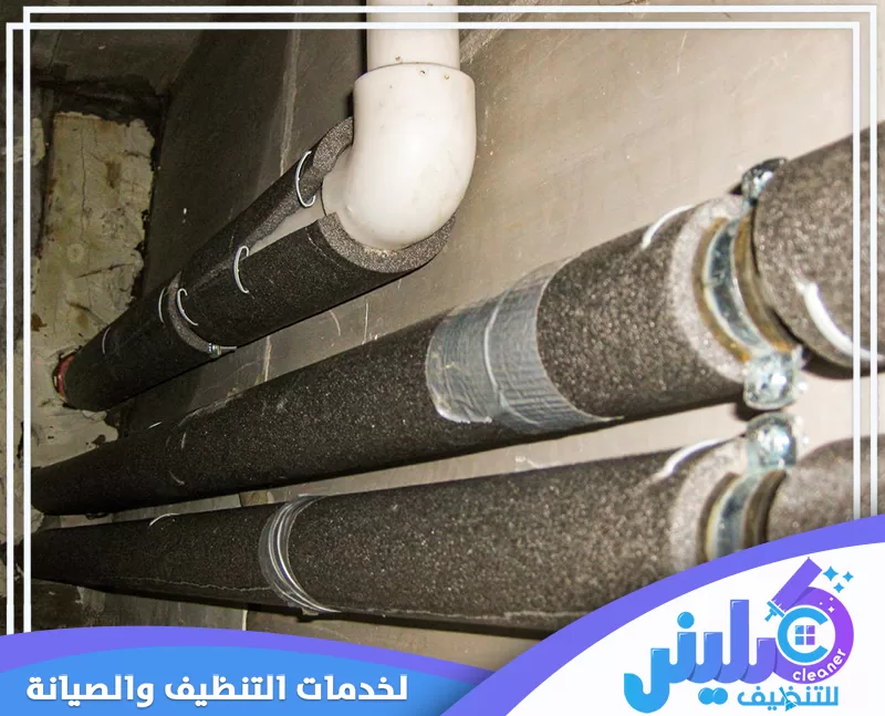 عزل مواسير التكييف والفريون بالرياض 0500892799 شركة كلينر. مواسير مياه معزولة بغطاء أسود مثبتة بمشابك معدنية داخل ممر ضيق، مع ظهور كوع ماسورة أبيض.