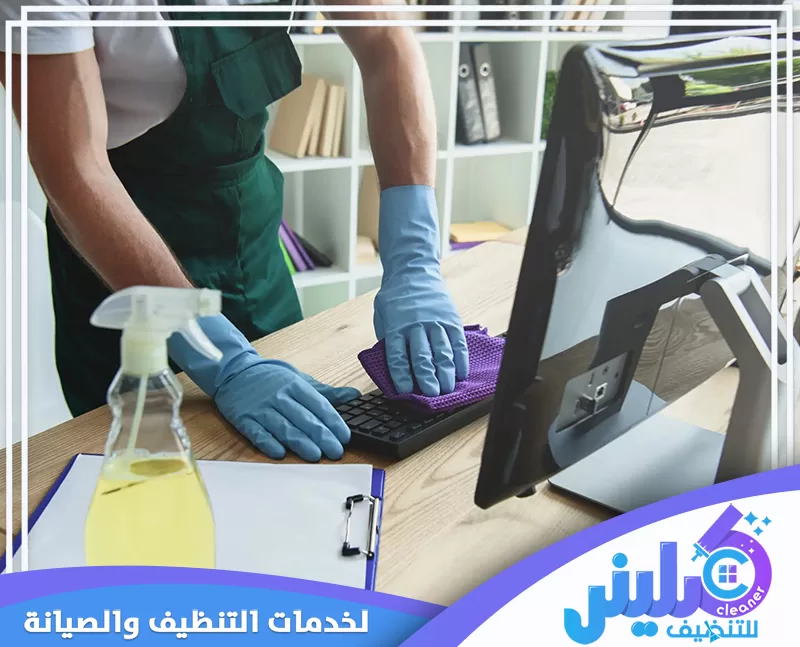 عامل تنظيف مكاتب ينظف لوحة مفاتيح الكمبيوتر والمكتب باستخدام أدوات ومنظفات مخصصة.